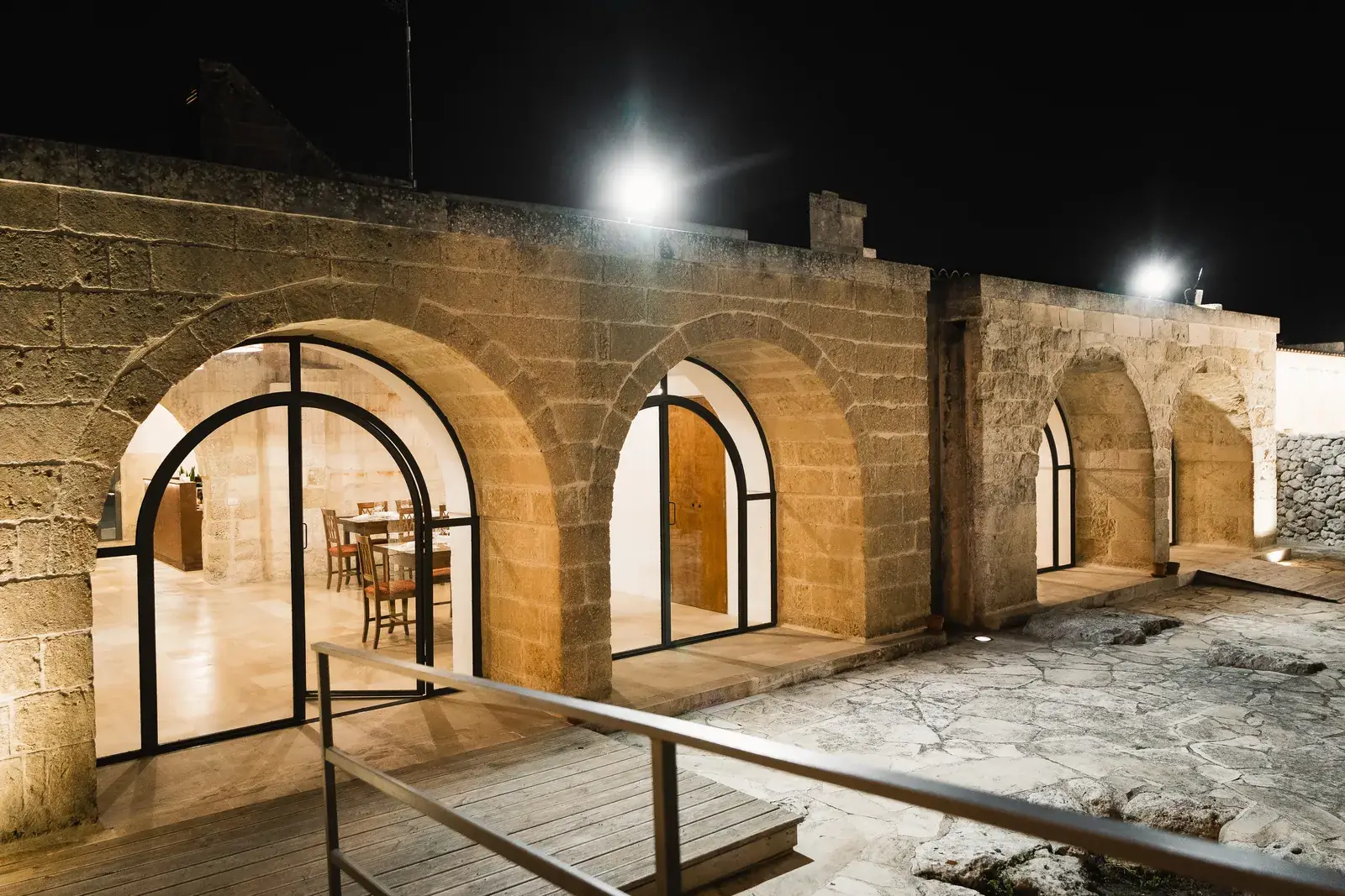 Gli archi in pietra della masseria illuminati di sera, con le vetrate aperte sulla corte
